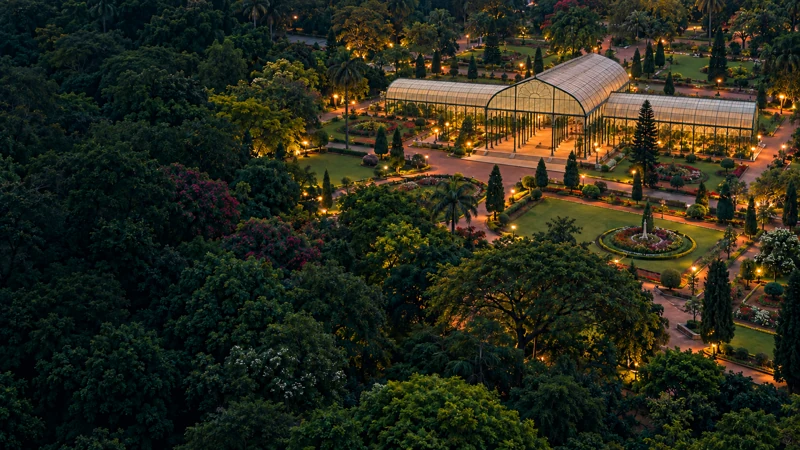 Artistic aerial impression of Lalbagh’s Glass House and tree canopy in Bengaluru at dusk.